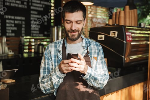 Preview: Portrait of caucasian barista guy typing on mobile phone in stre