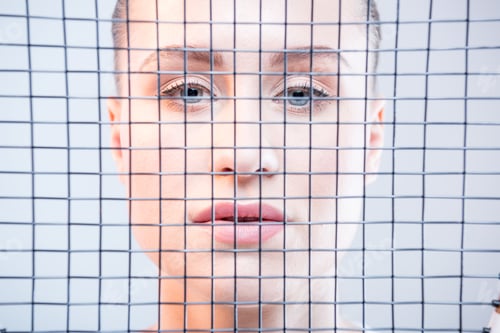 Preview: Gorgeous young woman looking at camera through tennis racquet