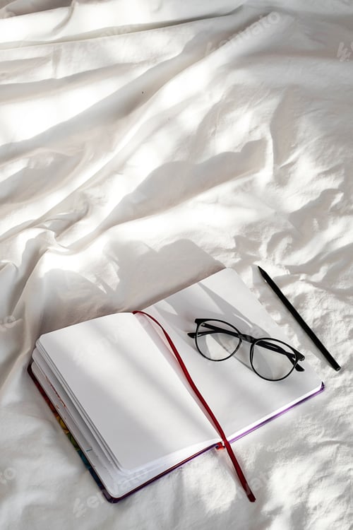 Preview: Blank Notebook, Pencil, Eyeglasses Rest on White Bedding in Sunlight with Shadows.