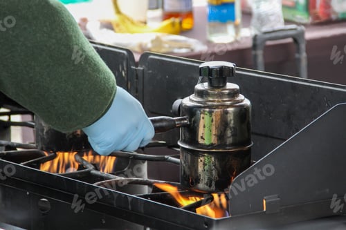 Preview: Person making coffee in a camping coffee pot on gas stove during winter outdoor event.