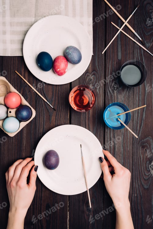 Preview: Woman painting eggs for Easter on wooden table