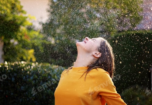Preview: Cheerful preteen girl catching rain drops outdoors