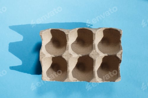 Preview: Empty eggs carton box with hard shadows on blue background.