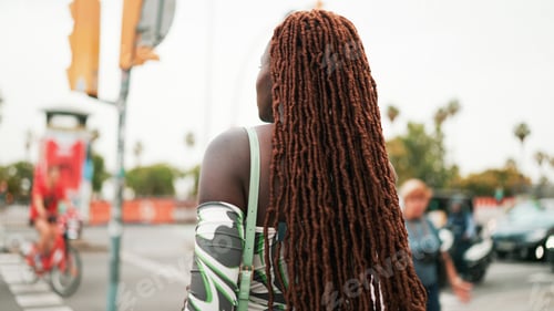 Preview: Woman with African braids wearing top crosses the road at crosswalk