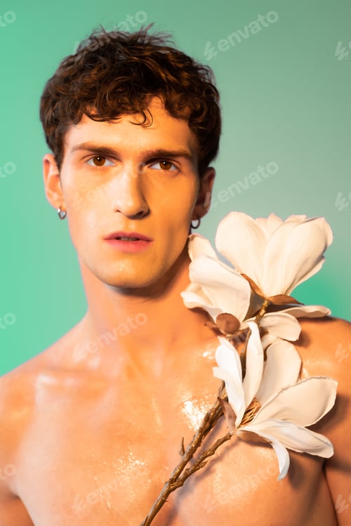Preview: Young model with oil on skin posing with magnolia branch on green background