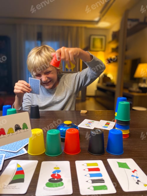 Preview: Game night, blond 9 years old boy playing board cozy dark room spending time together,apartment life