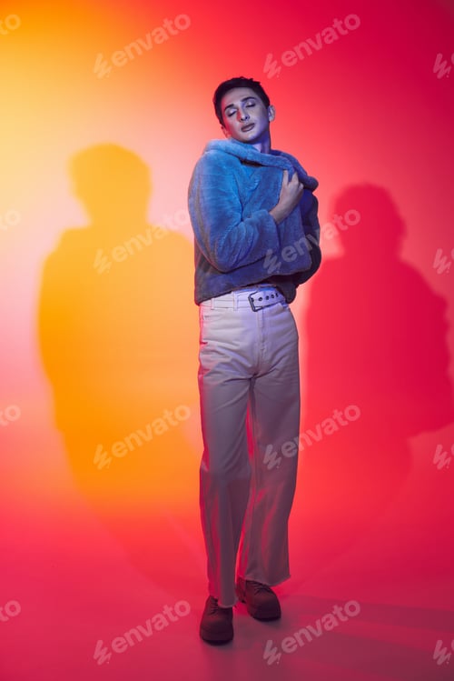 Preview: fancy alluring androgynous man in purple faux fur posing with closed eyes on vibrant backdrop