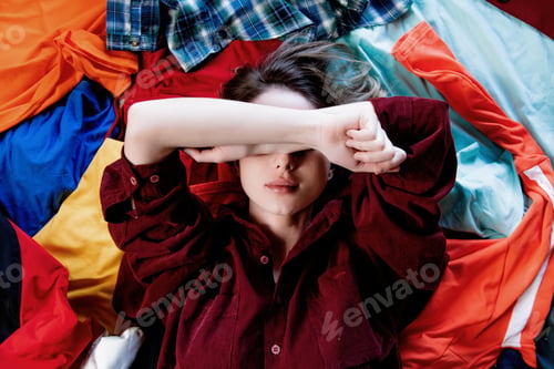 Preview: Upset woman keep hands over head and lying on clothes.