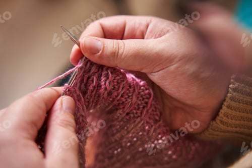 Preview: hands of a knitter close-up. A young girl knits knitting needles from pink yarn.