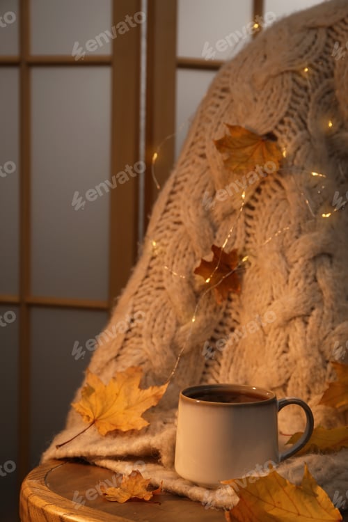 Preview: Cup of aromatic tea, sweater and autumn leaves on wooden chair indoors, space for text