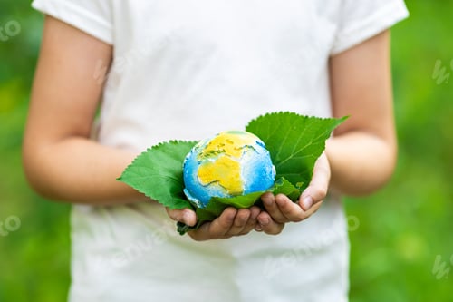 Preview: Kid holding small planet in hands against spring or summer green background. Ecology, environment