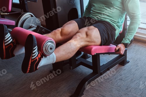 Preview: Active man is doing legs exercises on training apparatus in gym