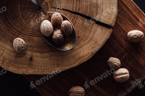 Preview: elevated view of cutting board and spoon with pile of nutmegs on wooden tabletop
