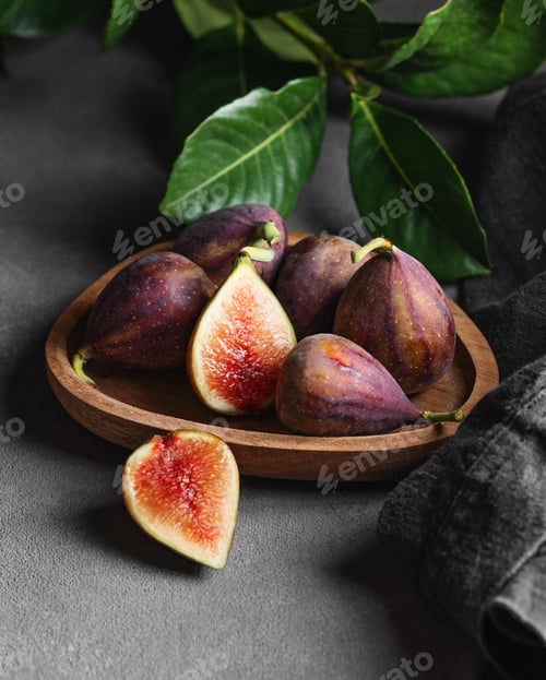 Preview: Juicy figs in a wooden plate on a dark background with leaves and a napkin.