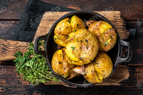 Preview: Crushed, Broken potatoes baked in oil with herbs. Wooden background. Top view