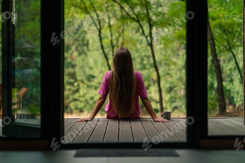 Preview: a young smiling woman sits sideways on a terrace overlooking the forest and enjoys the silence