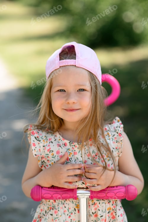 Preview: A little girl 3 years old in a pink cap rides a scooter. Summer time.