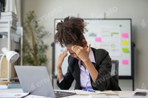 Preview: Young businesswoman is suffering from a headache while working on her laptop at her desk