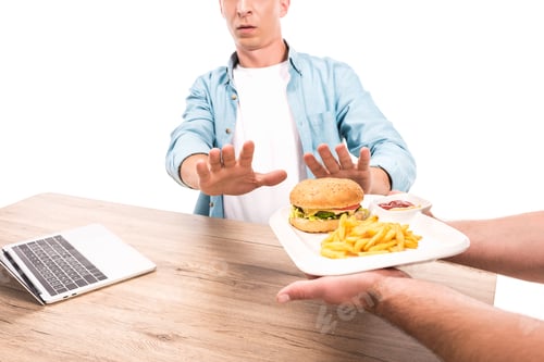 Preview: cropped image of man rejecting unhealthy burger and french fries at table isolated on white