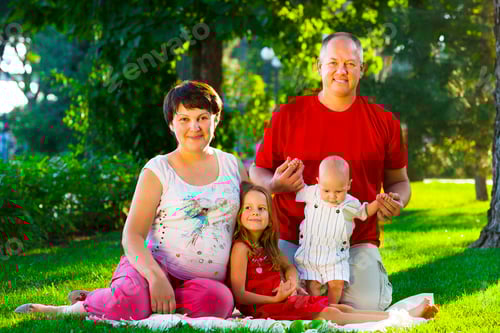 Preview: Happy family with two children sitting on green grass