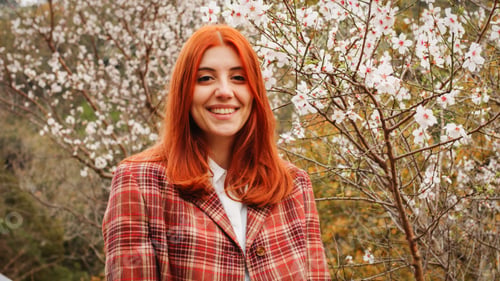 Preview: Happy red-haired girl under spring flower tree. Spring mood.
