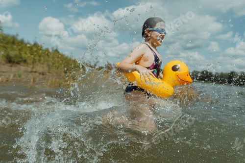Preview: Cheerful child playing by the lake with an inflatable yellow duck on a bright day