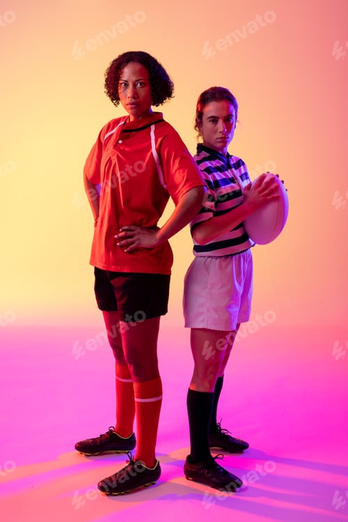 Preview: Portrait of two diverse female rugby players with rugby ball over neon pink lighting