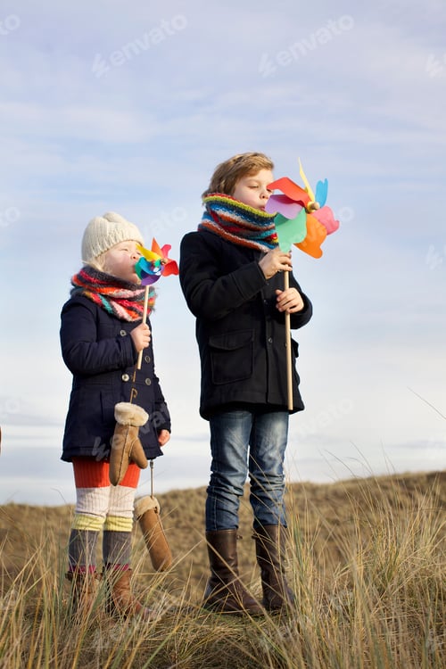 Preview: Brother and sister blowing on paper windmills at coast