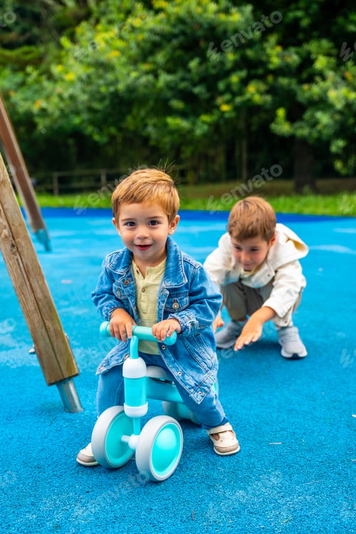 Preview: Toddler boy riding balance bike at playground with older brother watching