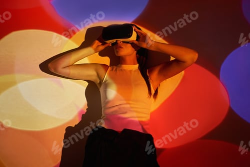 Preview: Confident young woman adjusting her virtual reality glasses against colorful background