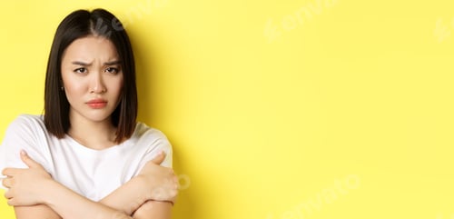 Preview: Sad timid girl comforting herself, hugging body and frowning upset, standing again yellow