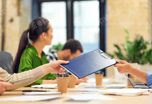 Preview: Male coworker giving a folder with documents to his colleague while working in the modern office