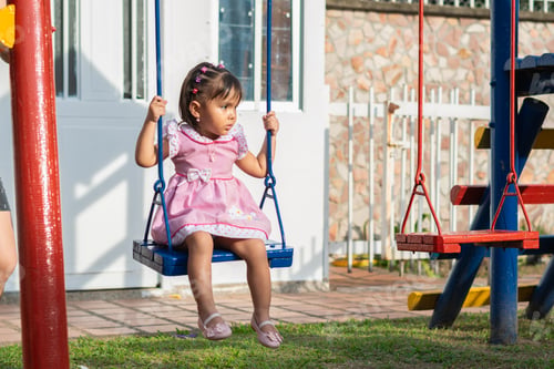 Preview: little latina girl sitting on the swing in the park looking to the side while she is rocking
