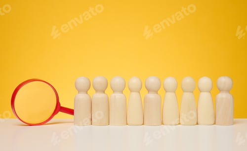 Preview: Wooden figures of men stand on a yellow background and a red plastic magnifying glass.