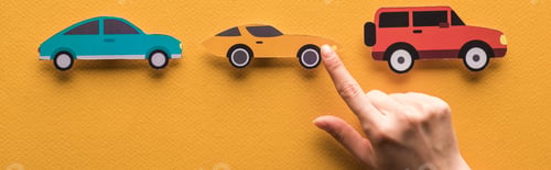Preview: cropped view of woman pointing with finger at paper cut cars on orange background, panoramic shot