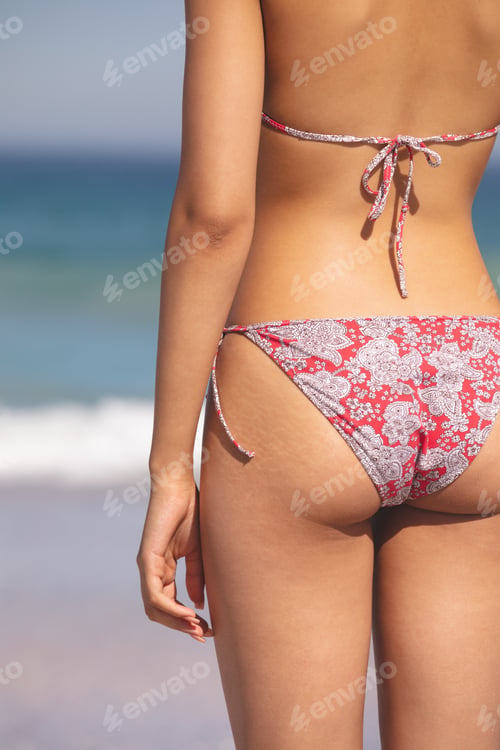 Preview: Mid section of mixed race woman in bikini standing on the beach