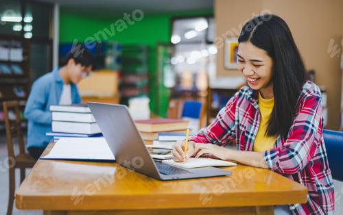 Preview: Female college student working on laptop and searching for books to study,