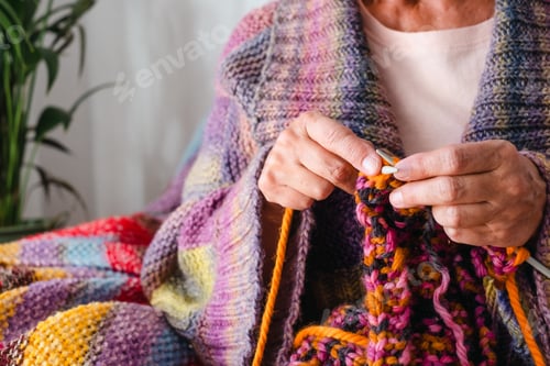 Preview: Close up on senior mature woman sitting on sofa at home while knitting. Work in progress.