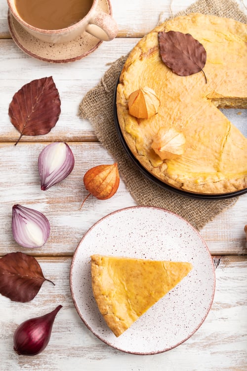 Preview: Autumn onion pie decorated with leaves and cup of coffee on white wooden background. Top view.