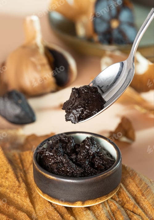 Preview: Spoon with black garlic paste. A small clay bowl with black aioli on a handmade wooden plate