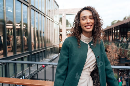 Preview: Portrait of young woman in green coat with curly hair in the city