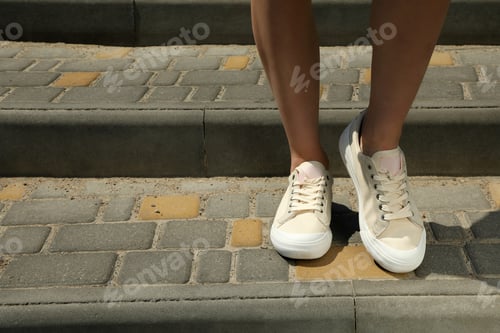 Preview: Stylish white sneakers on women's legs on cobblestones