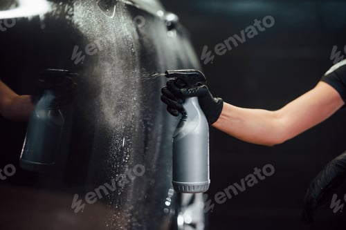Preview: Spraying the vehicle. Modern black automobile get cleaned by woman inside of car wash station
