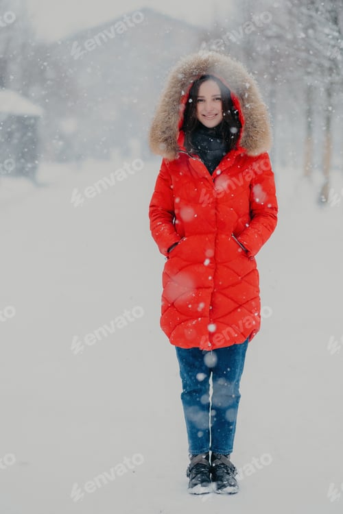 Preview: Woman wears red winter jacket, jeans and boots, keeps hands in pockets