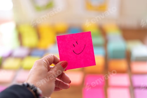Preview: Woman’s hand holding a colorful pink sticky note with a smile drawn on it