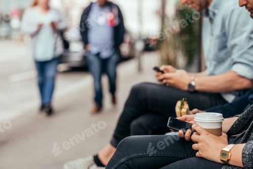 Preview: People sitting by city street using smart phones