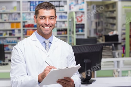 Preview: Middle-aged male pharmacist holding clipboard behind pharmacy counter near computer and shelves