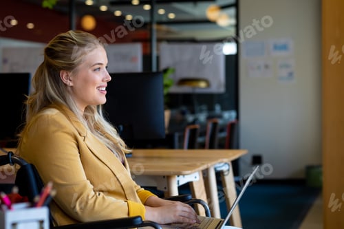 Preview: Happy plus size caucasian casual businesswoman in wheelchair using laptop in office