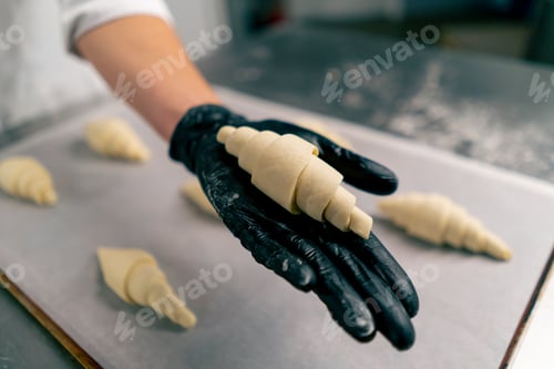 Preview: baker's hands placing shaped uncooked croissants on a baking sheet with parchment baking in the oven