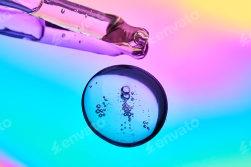 Preview: A drop of cosmetic serum and a pipette on a multicolored background in shades of blue and lilac.
